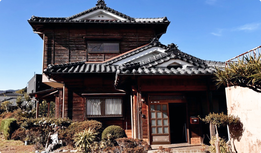 Two-storey wood akiya with dark tiled roof under a clear blue sky